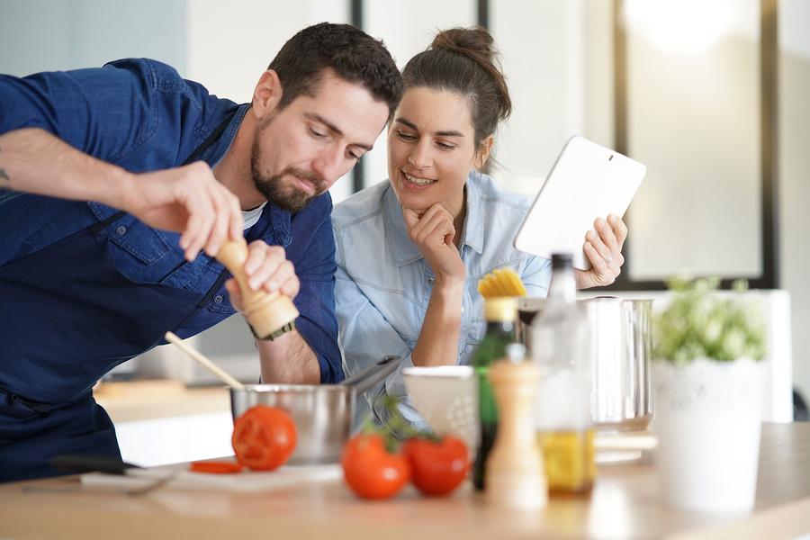 Couple cooking in kitchen, reading recipe on tablet