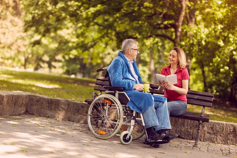 Young carer woman reading book  outdoor  to senior man 