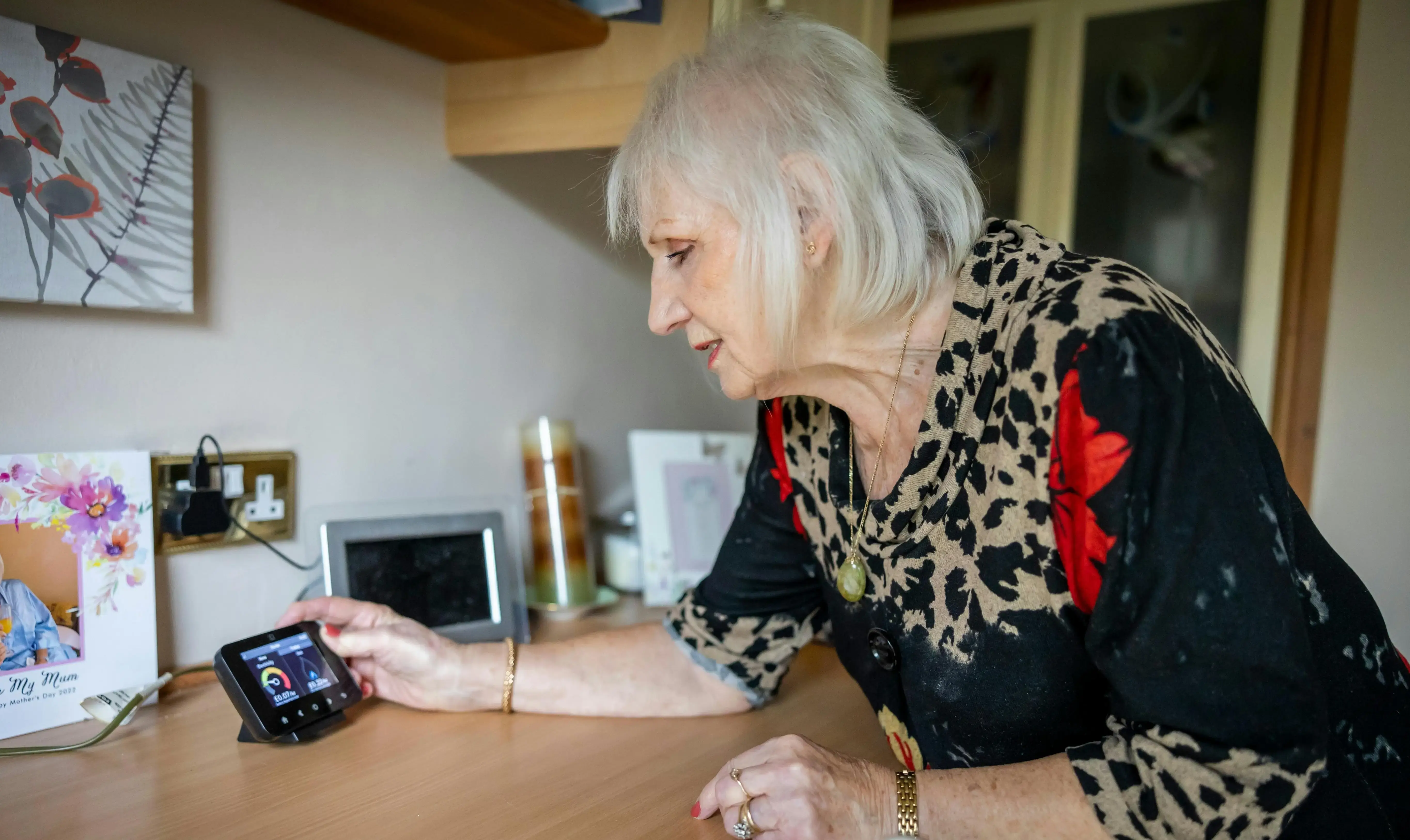 A older woman leaning over a desk, looking at a monitor on her phone. 